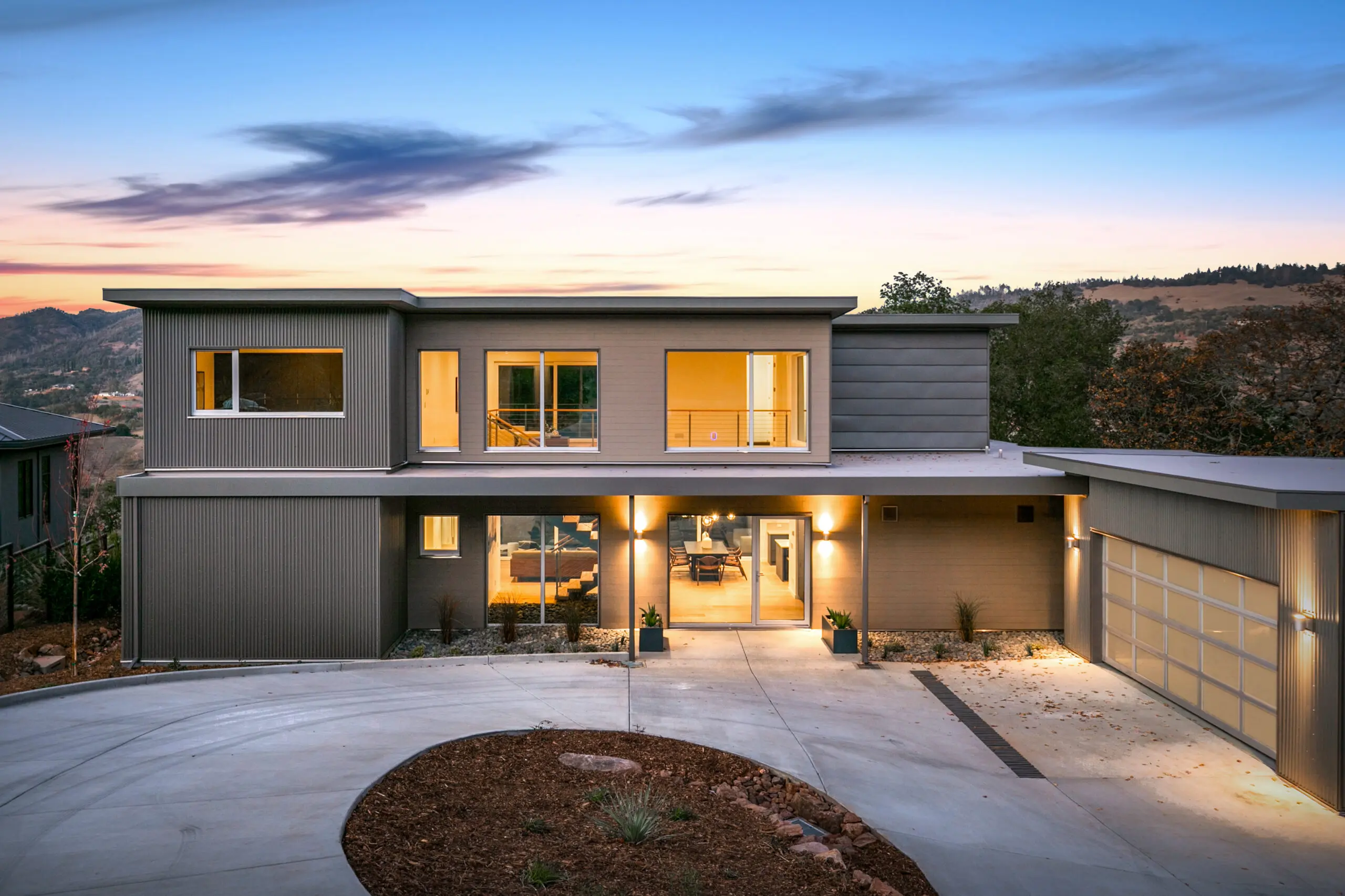 2-story modern home with circular drive; sunset a scrub landscape in the background. Modular home by Dvele.