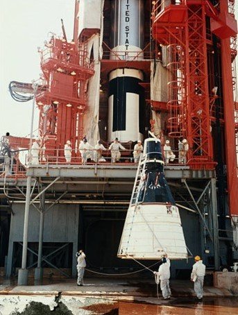 An image of a conical white and black spacecraft being lifted at a launch pad with a red gantry.