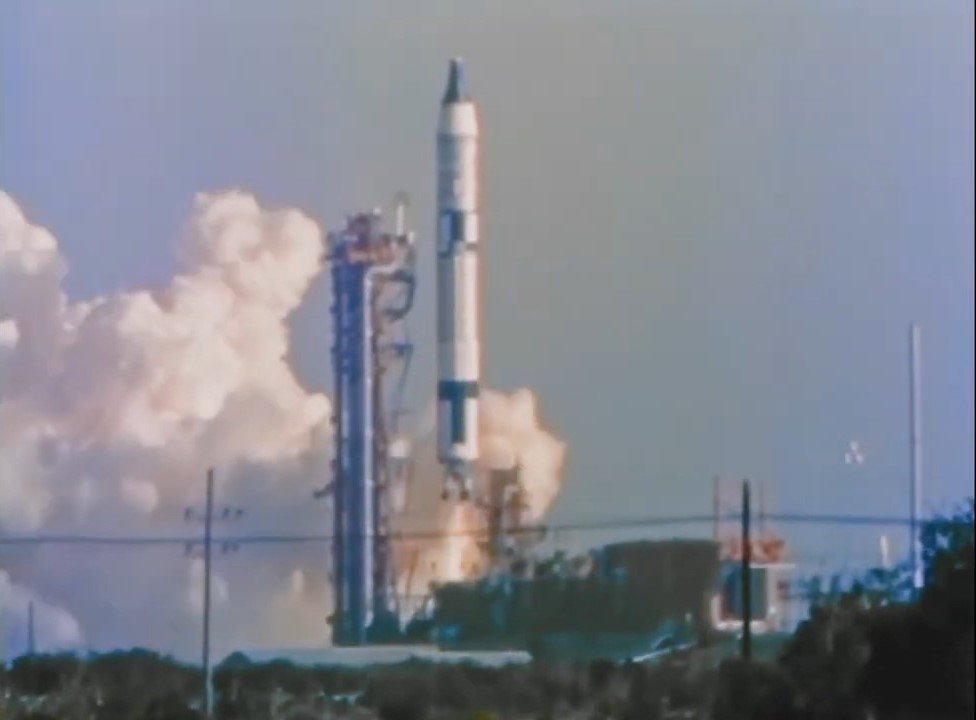 A white, gray, and black rocket lift off on a pillar of flame.