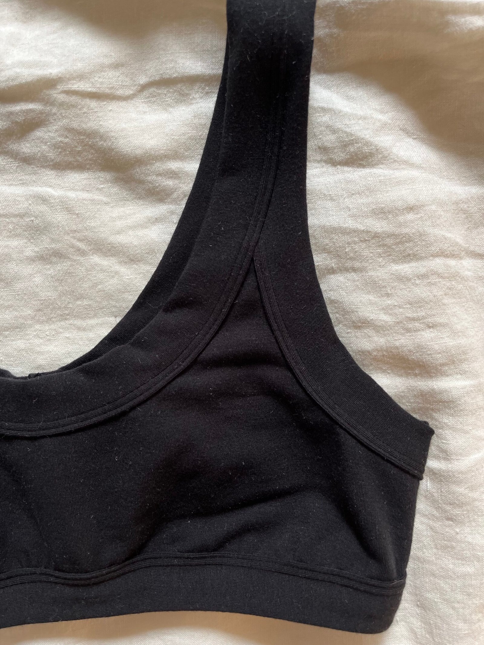 A black sports bra laid on a white fabric surface, displaying the left shoulder strap and part of the front.