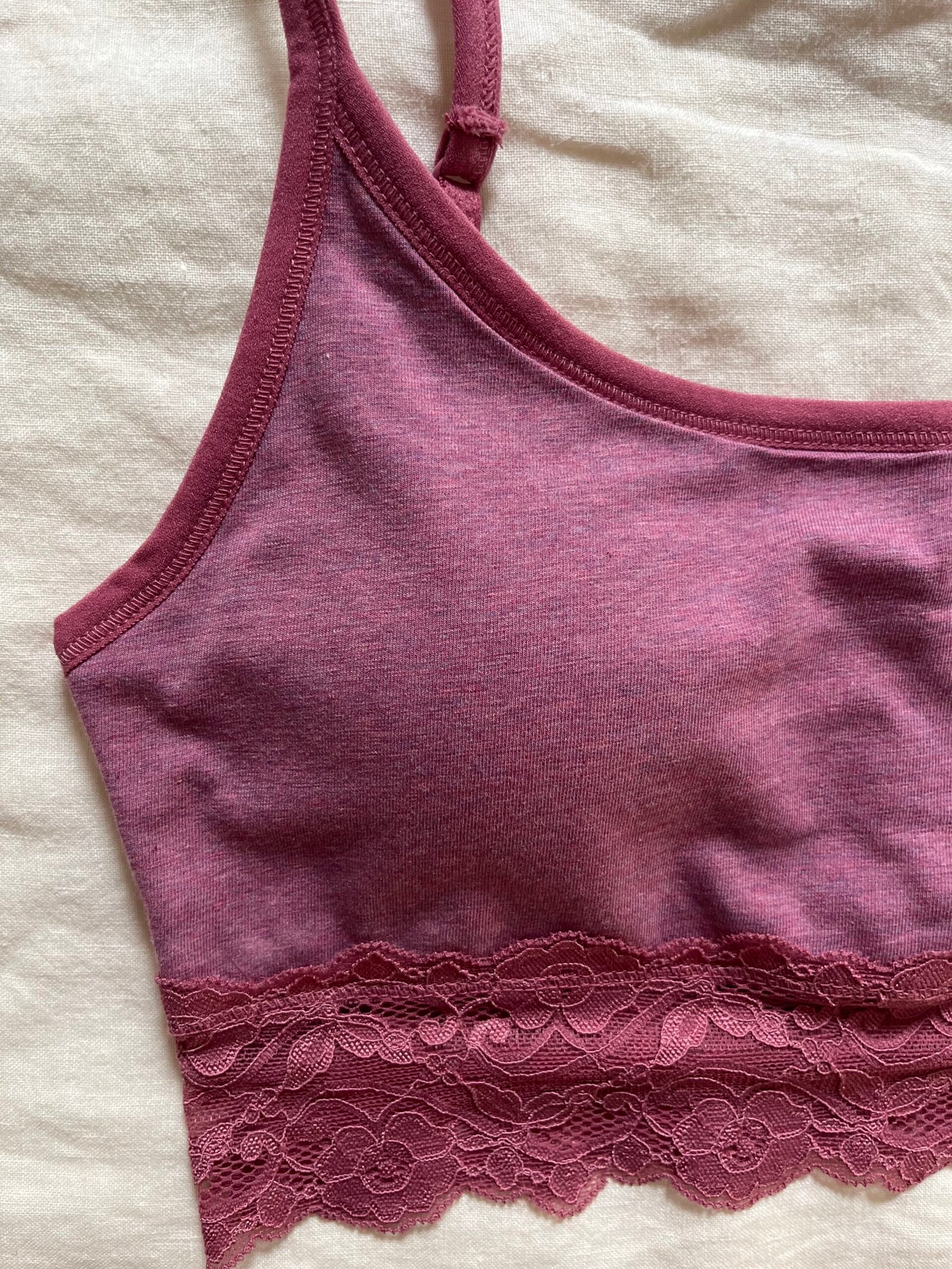 Close-up of a maroon bralette with lace trim at the bottom, laid flat on a beige fabric background.