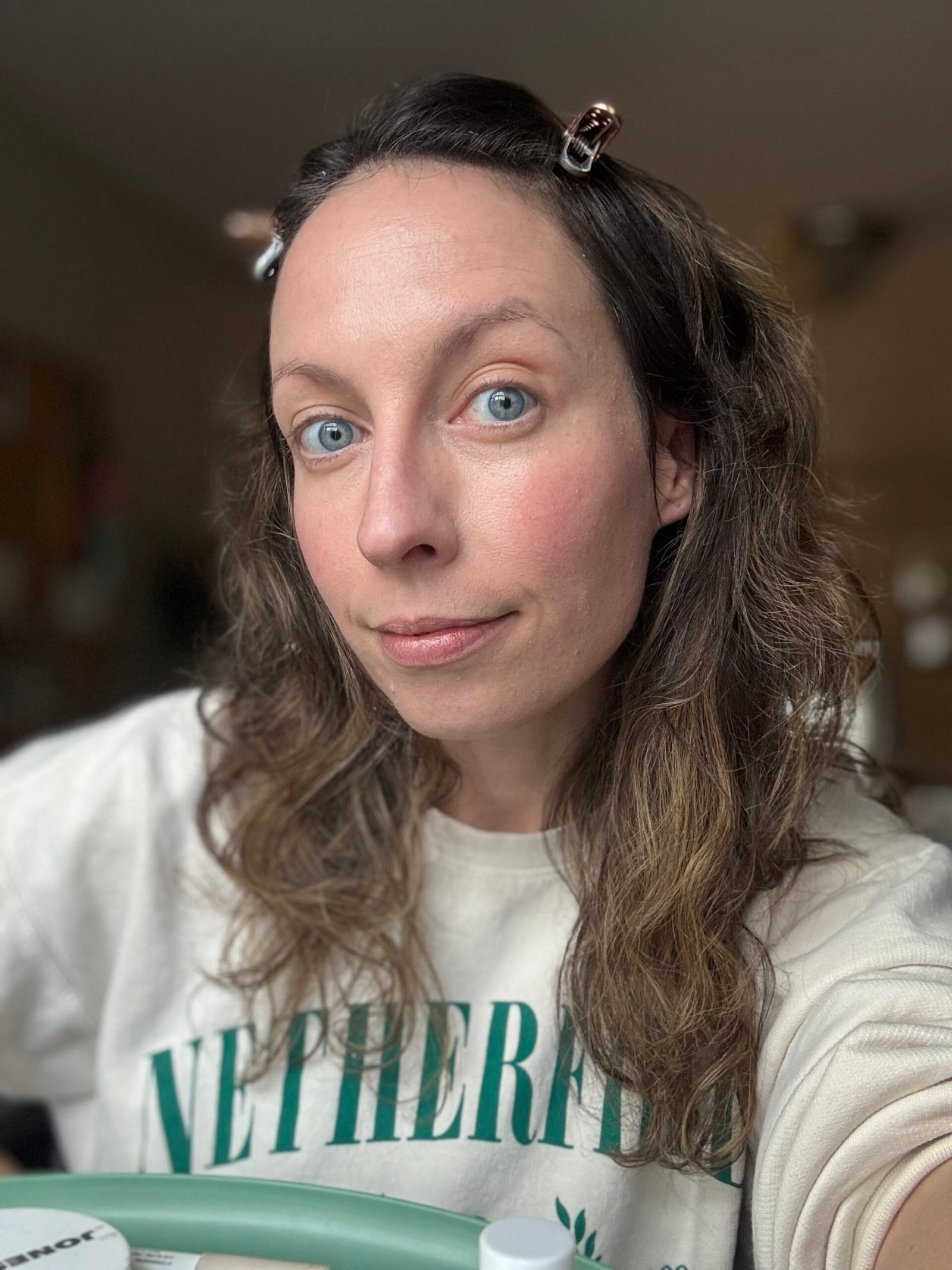 A person with long wavy hair adorned with stylish clips in a casual top gazes at the camera with a neutral expression indoors.