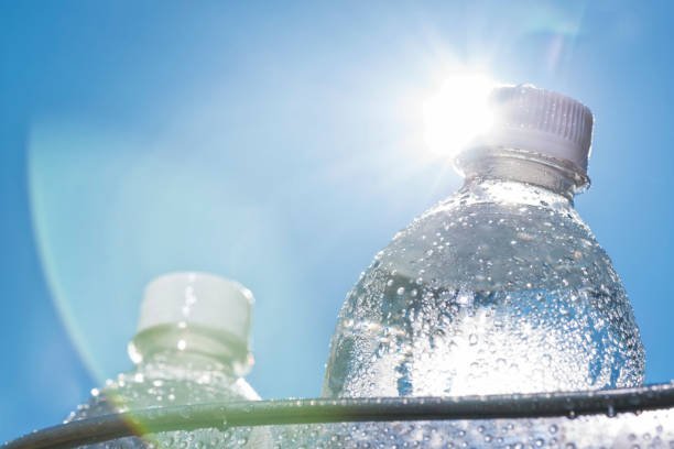 A close-up of a plastic water bottle in a bucket of ice as the Sun shines down on a hot Summer day. It is a good idea to keep hydrated while doing activities on a hot day.