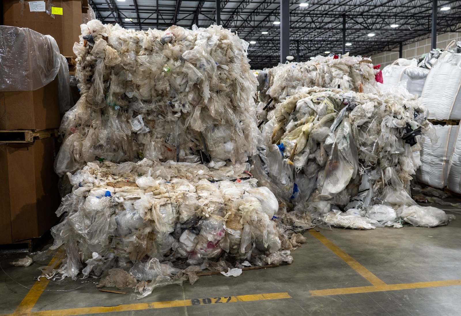 Bales of flimsy plastic trash sit on the floor of a warehouse