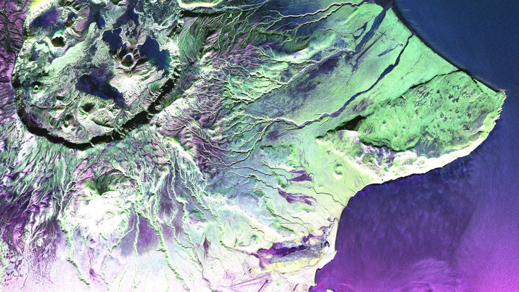 A close-up satellite image of a volcanic landscape with vibrant colors highlighting different geological features like craters, lava flows, and surrounding terrain.