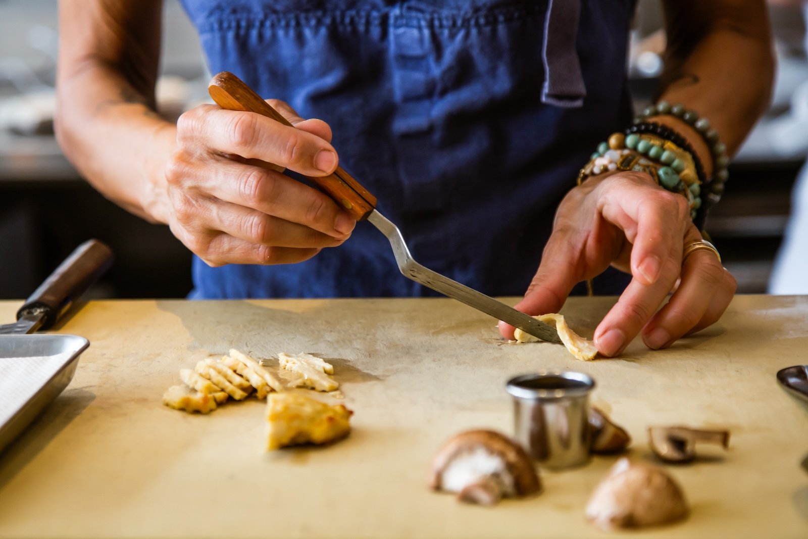 Chef Dominique Crenn uses a spatula to lift a small piece of lab-grown chicken on a cutting board.
