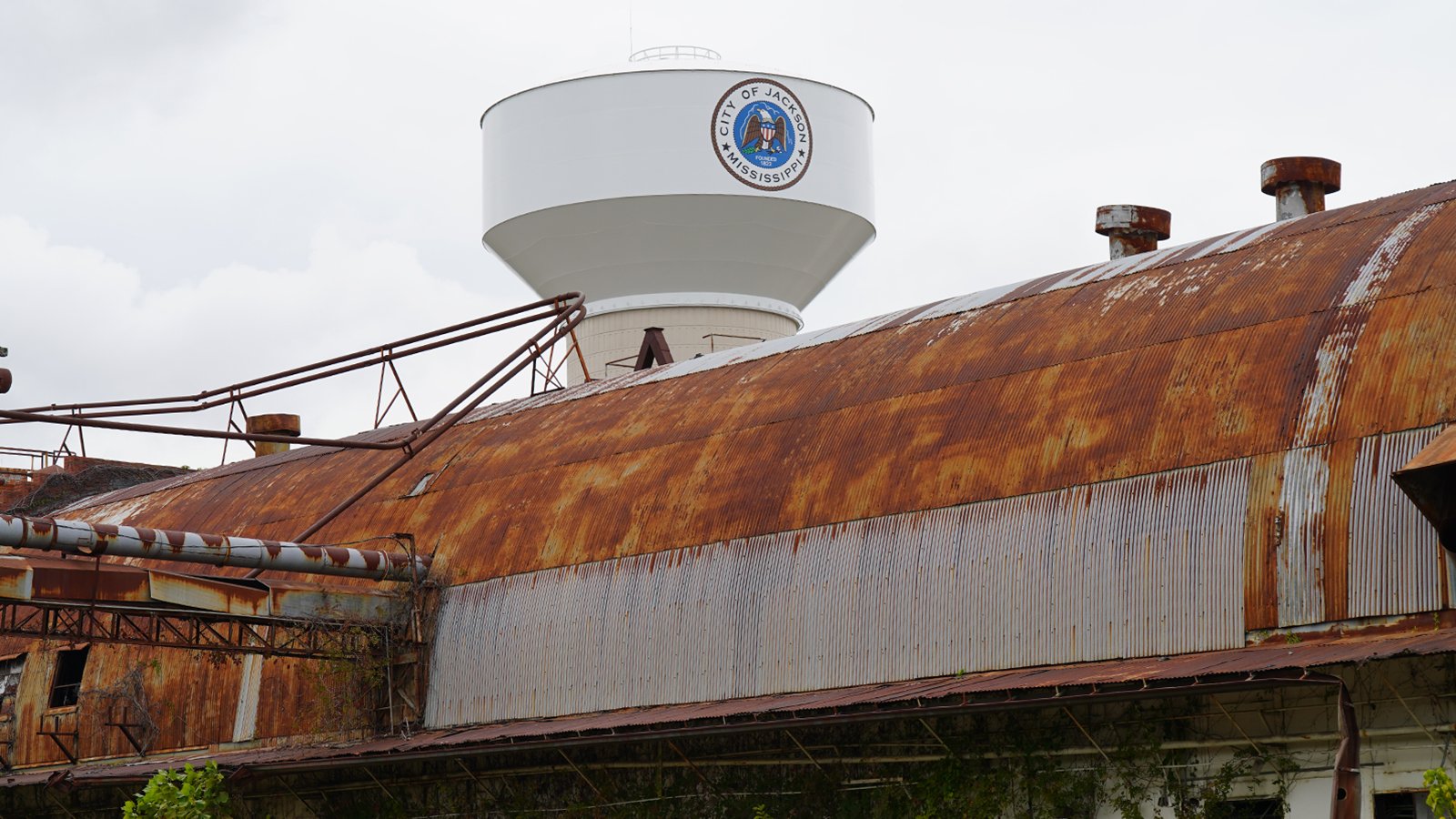 A water tower that says 'Jackson' near a rusty building