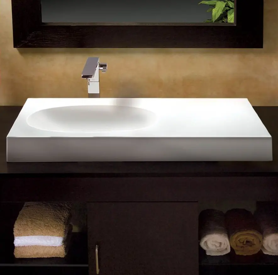 Oblong combined bathroom sink and counter rise a few inches from wood vanity; cubbies with rolled towels below and wood-frame mirror above. 