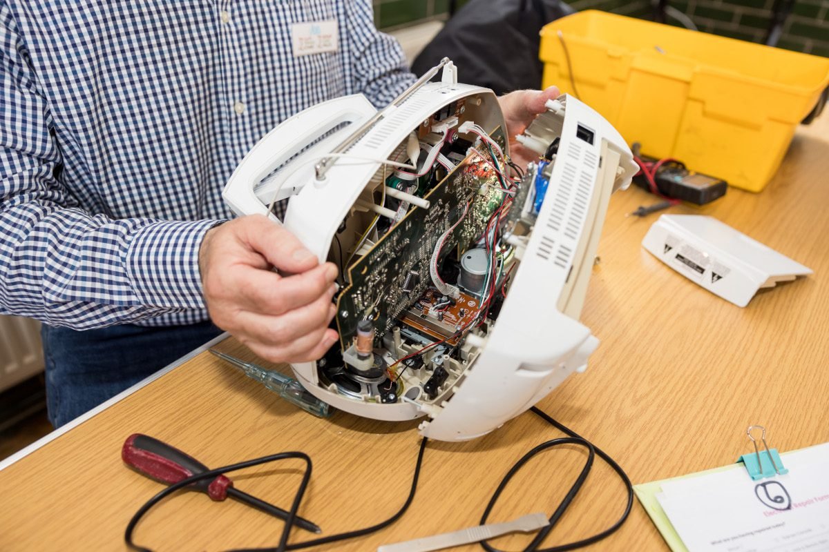 Someone opening up a white plastic appliance - possible a heater - to reveal the circuit boards inside