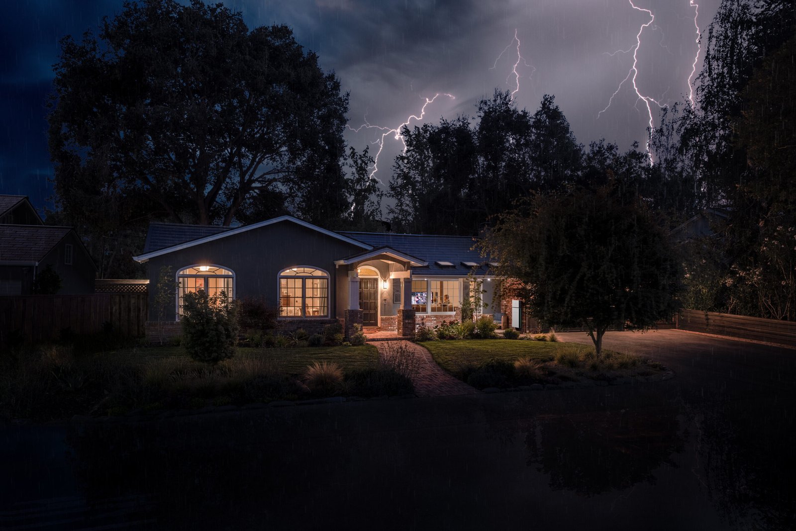 exterior view of home at night; lights glow warmly from withing while lighting storm light up the sky in the background - photo