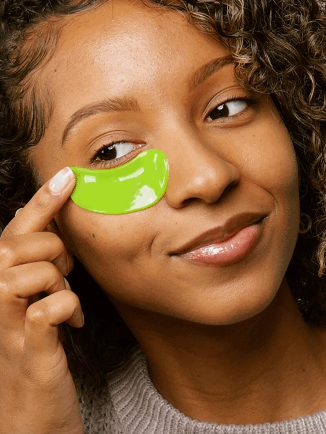 A person applying a green under-eye gel patch.