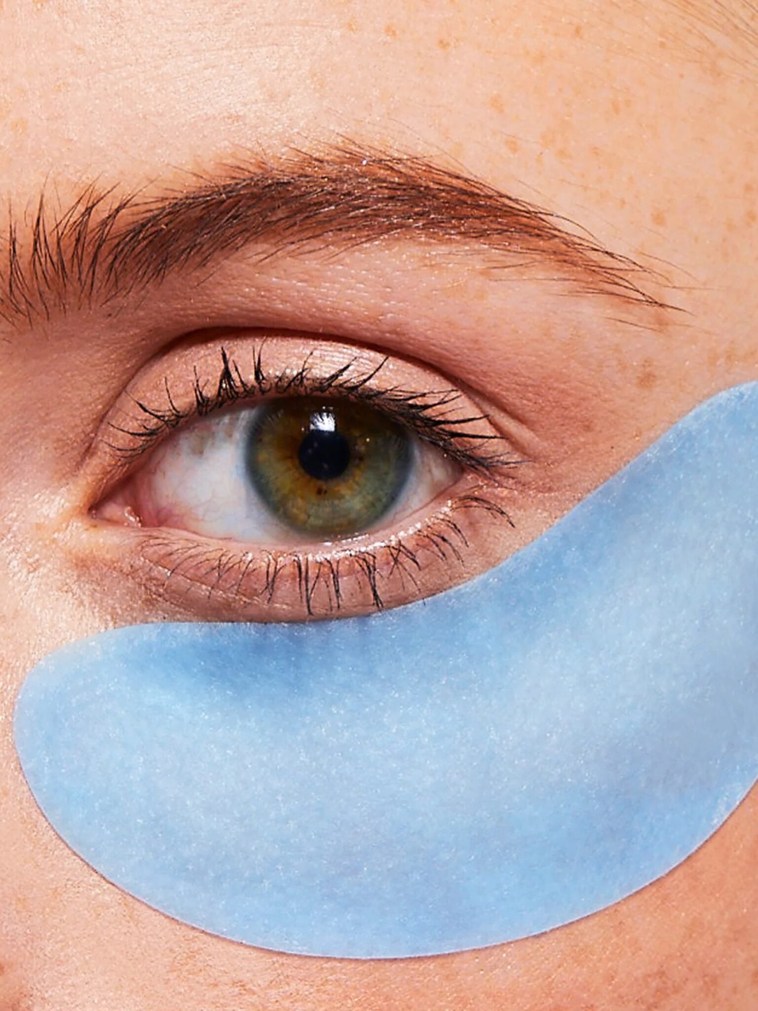 Close-up of a person's eye with a blue under-eye gel patch applied on the skin below.