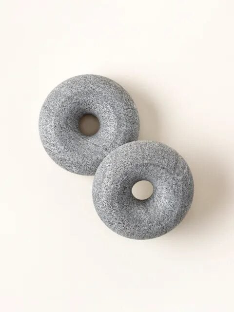 Two round, grey pumice stones with central holes are placed on a light background.