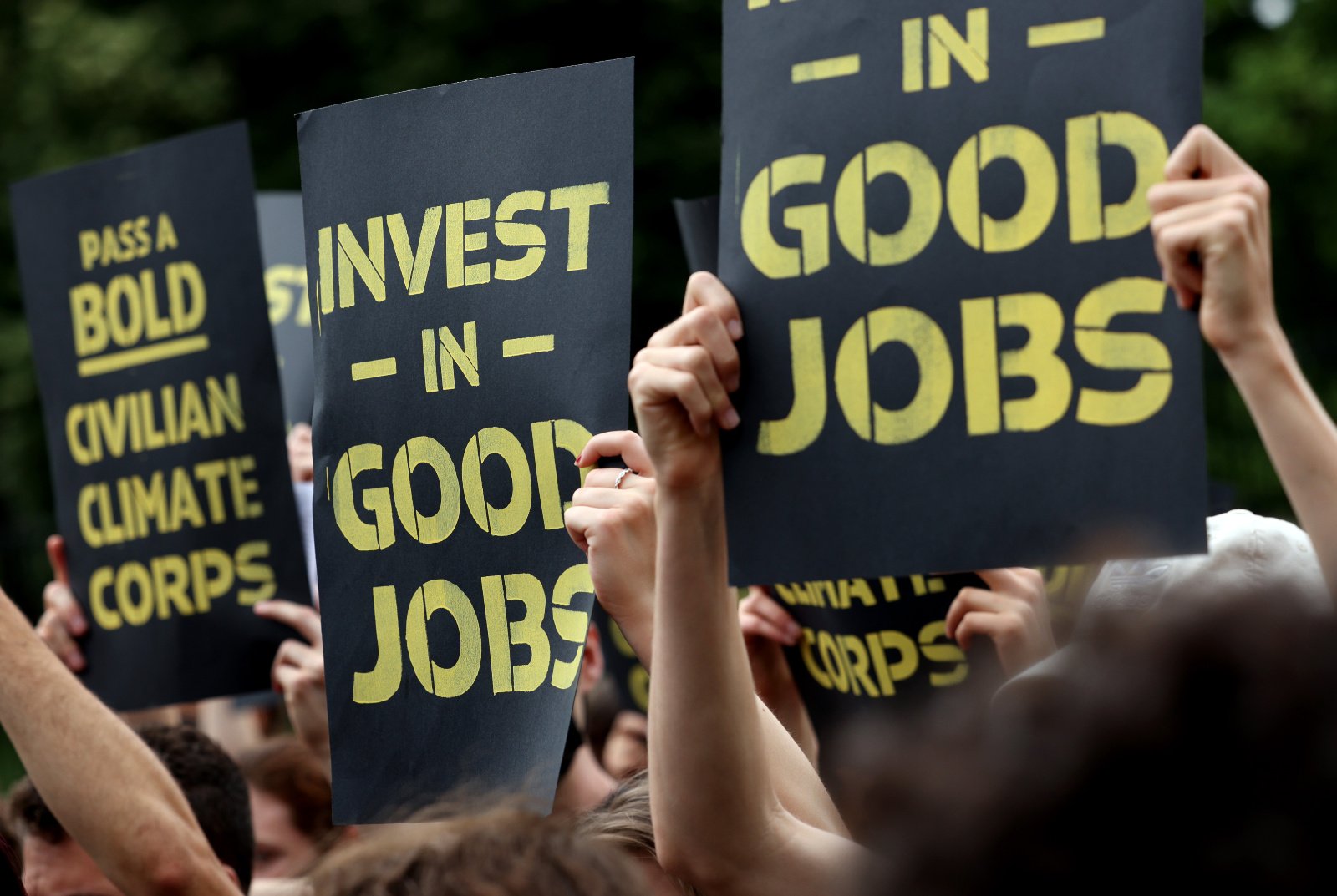 Close-up photo of people holding signs about investing in good jobs and a Civilian Climate Corps