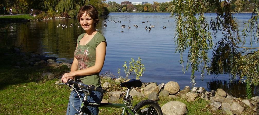 A person smiles next to a bicycle with waterfowl and Ottawa's Rideau Canal in the background