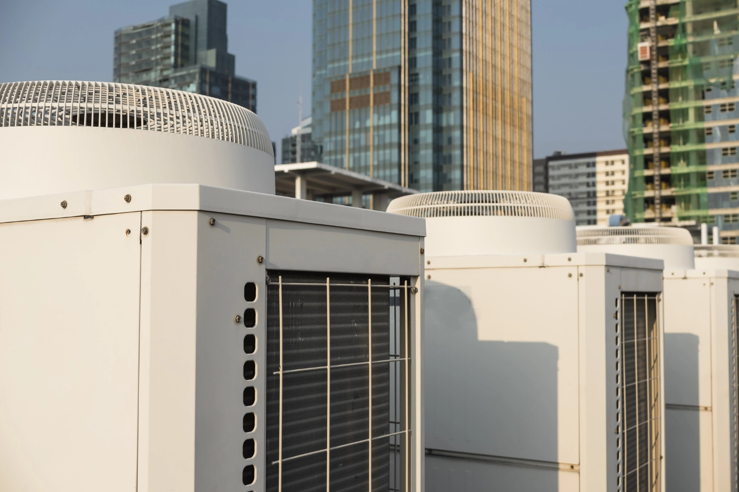 Pictures of Multiple Air Con units on a roof in Melbourne. The Air conditioners are shown close in the foreground with Melbourne skyscrapers are shown in the background