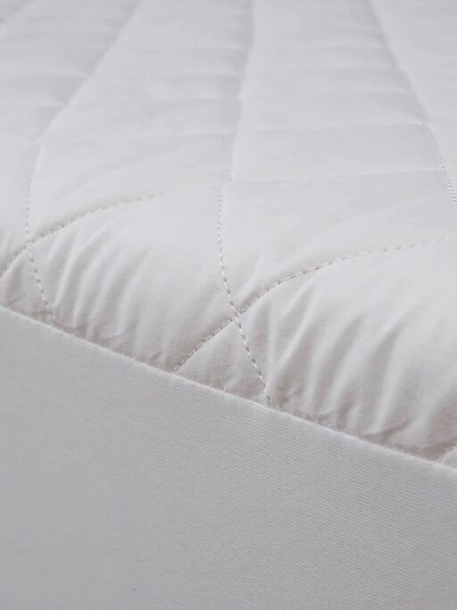 Close-up of a white quilted mattress corner with a textured surface and a fabric border.
