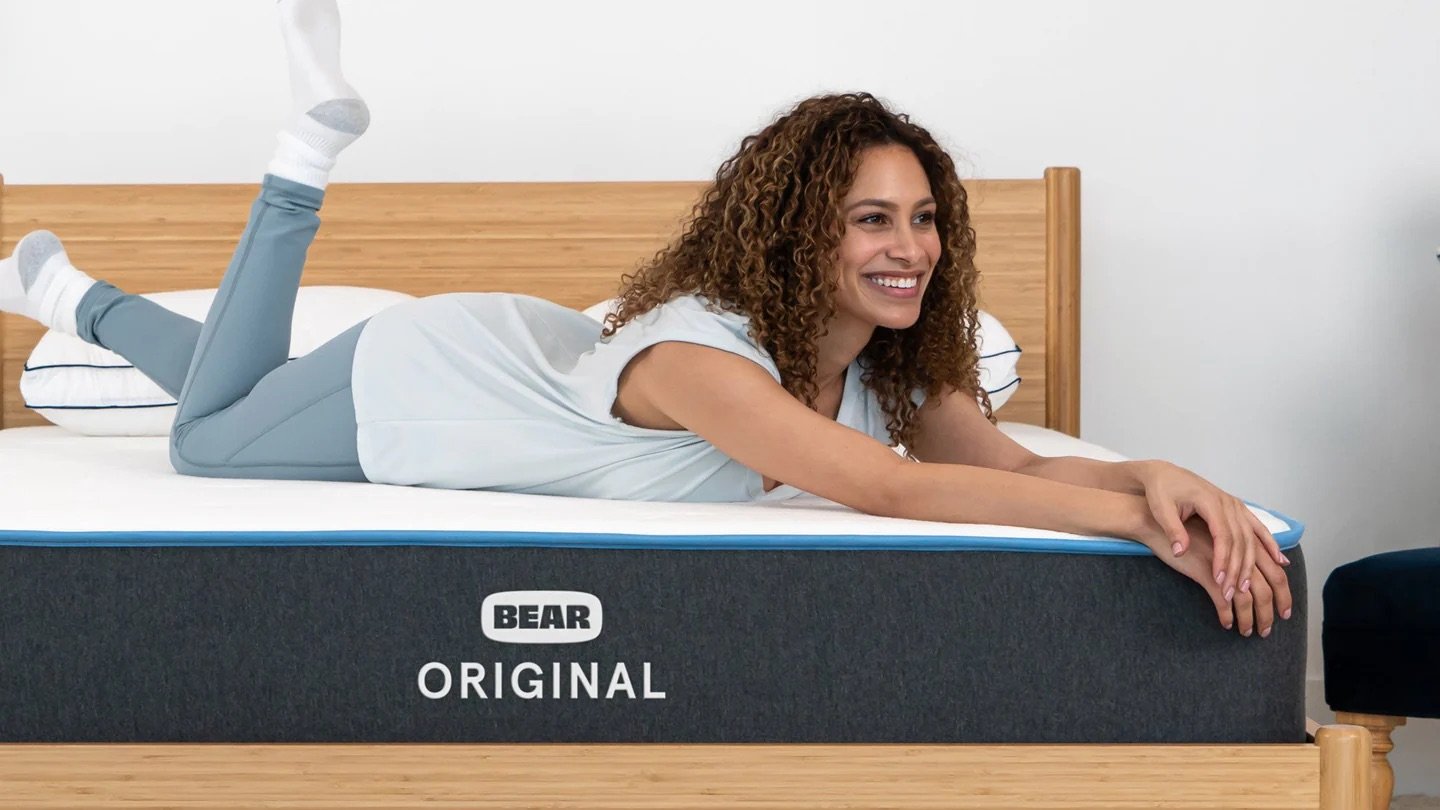 A person is lying on a Bear Original nontoxic mattress, smiling with arms and legs extended.