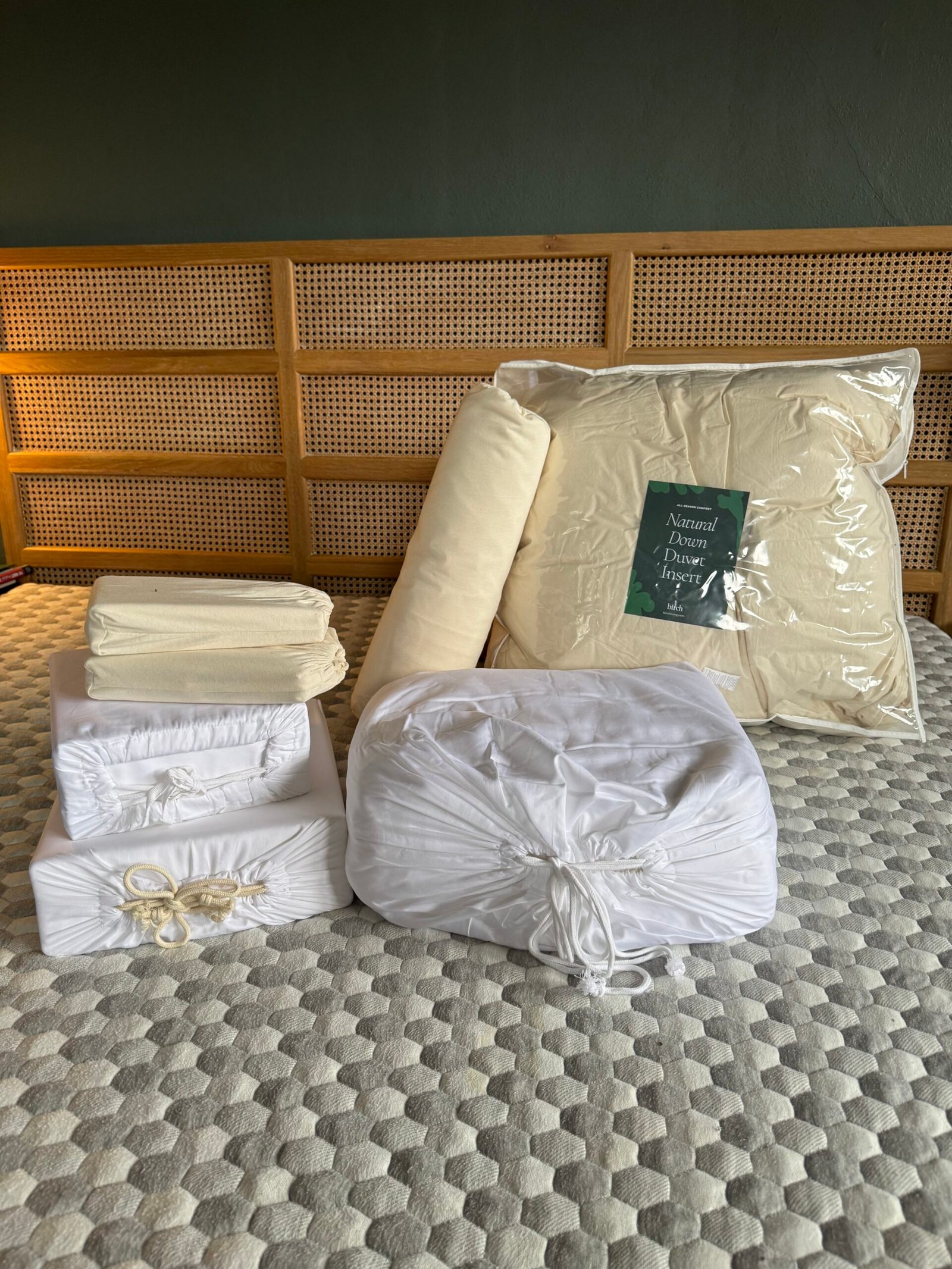 A collection of neatly packaged white bedding items, including duvets, sheets, and pillowcases, arranged on a textured gray surface with a wooden backdrop.