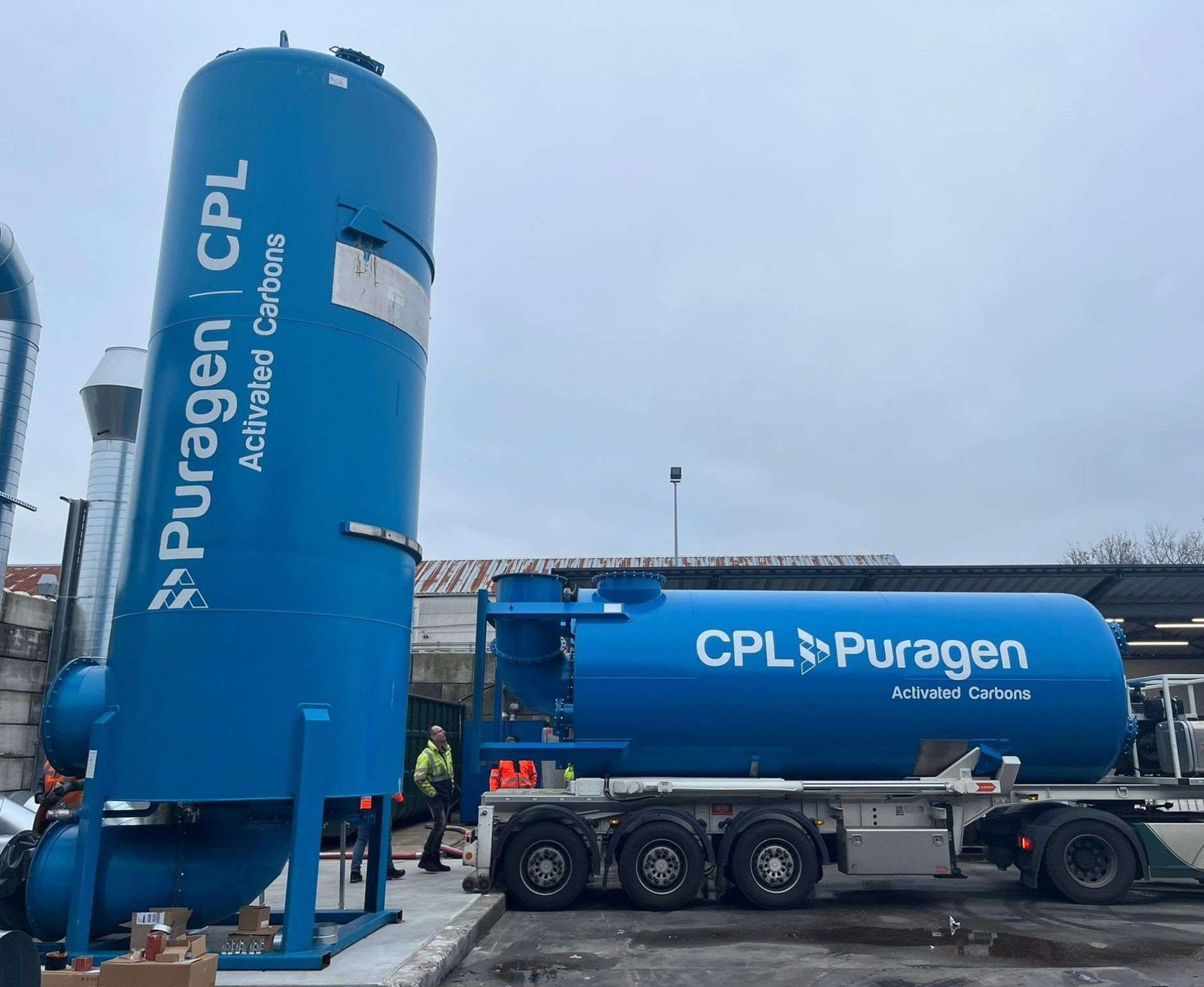 A tall vertical storage tank and a tanker vehicle, both bearing the legend 