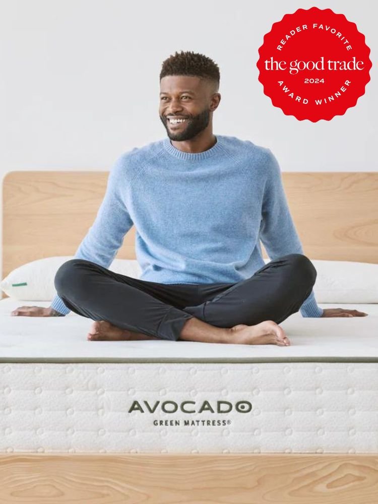 A man sits cross-legged on an Avocado Green Mattress, proudly displaying "The Good Trade 2024 Reader Favorite Award Winner" badge. This organic mattress is celebrated in many a nontoxic mattress review for its exceptional quality and comfort.