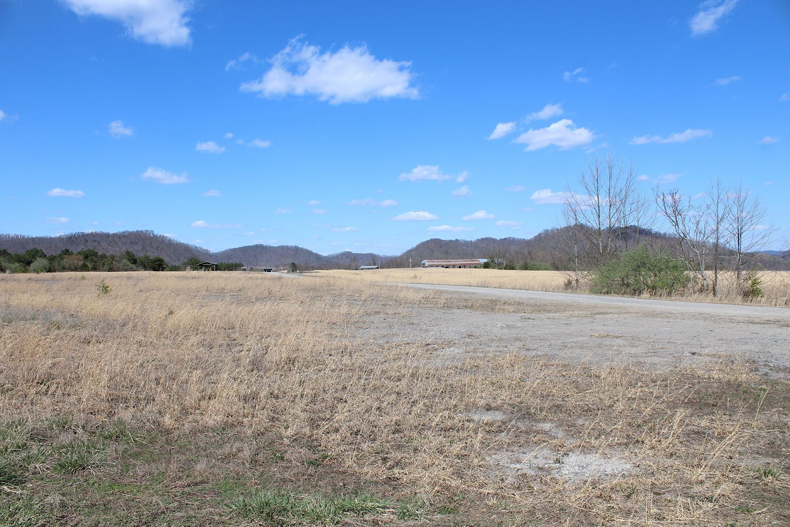 A flat field of short brown grass is seen beneath a blue sky with mountains in the background.