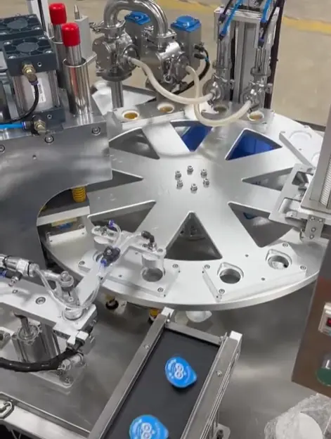 Rotary cup filling machine with stainless steel nozzles filling plastic cups on a rotary platform.