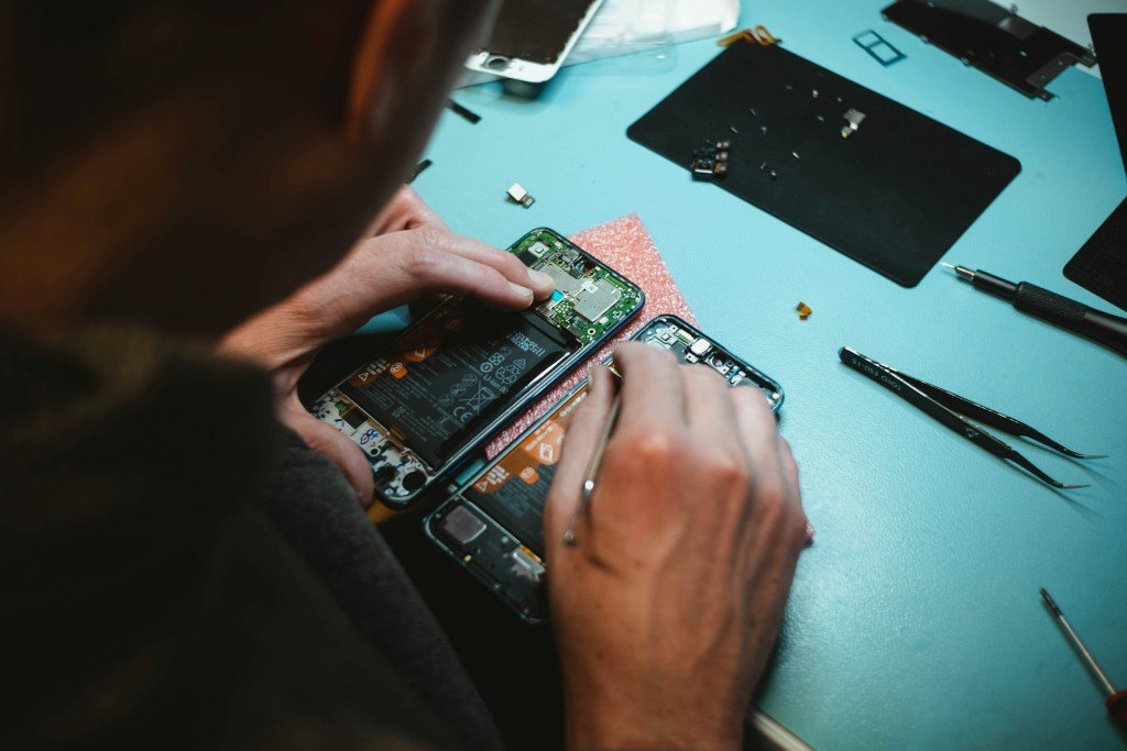 A close-up image of someone repairing a phone, replacing a component, extending the life cycle of the product and resisting planned obsolescence.