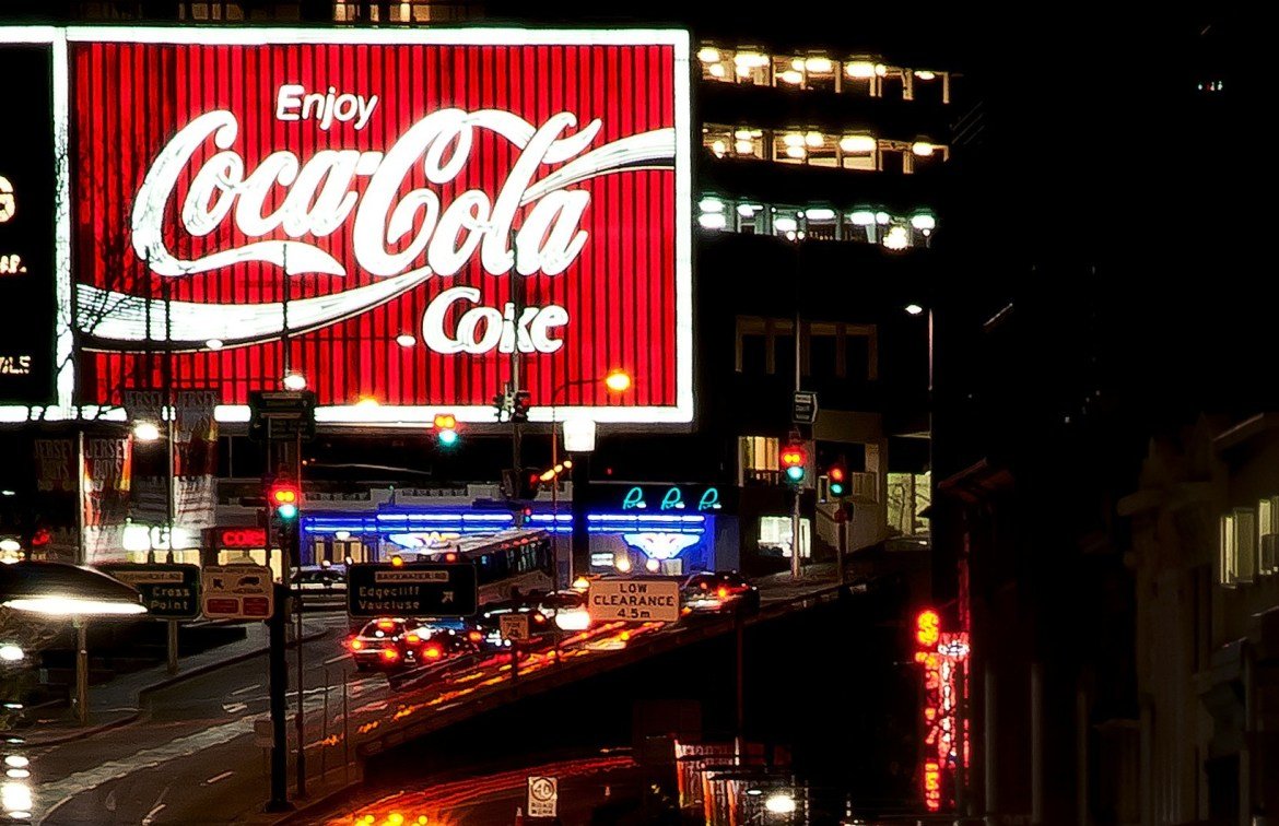 Large digital ad for Coca Cola over a busy highway at night. 