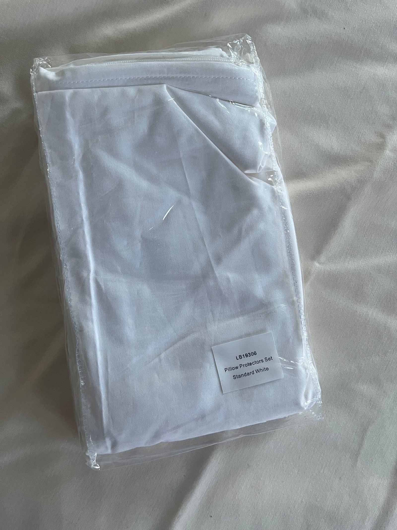 A packaged white pillow protector set is placed on a light-colored surface.
