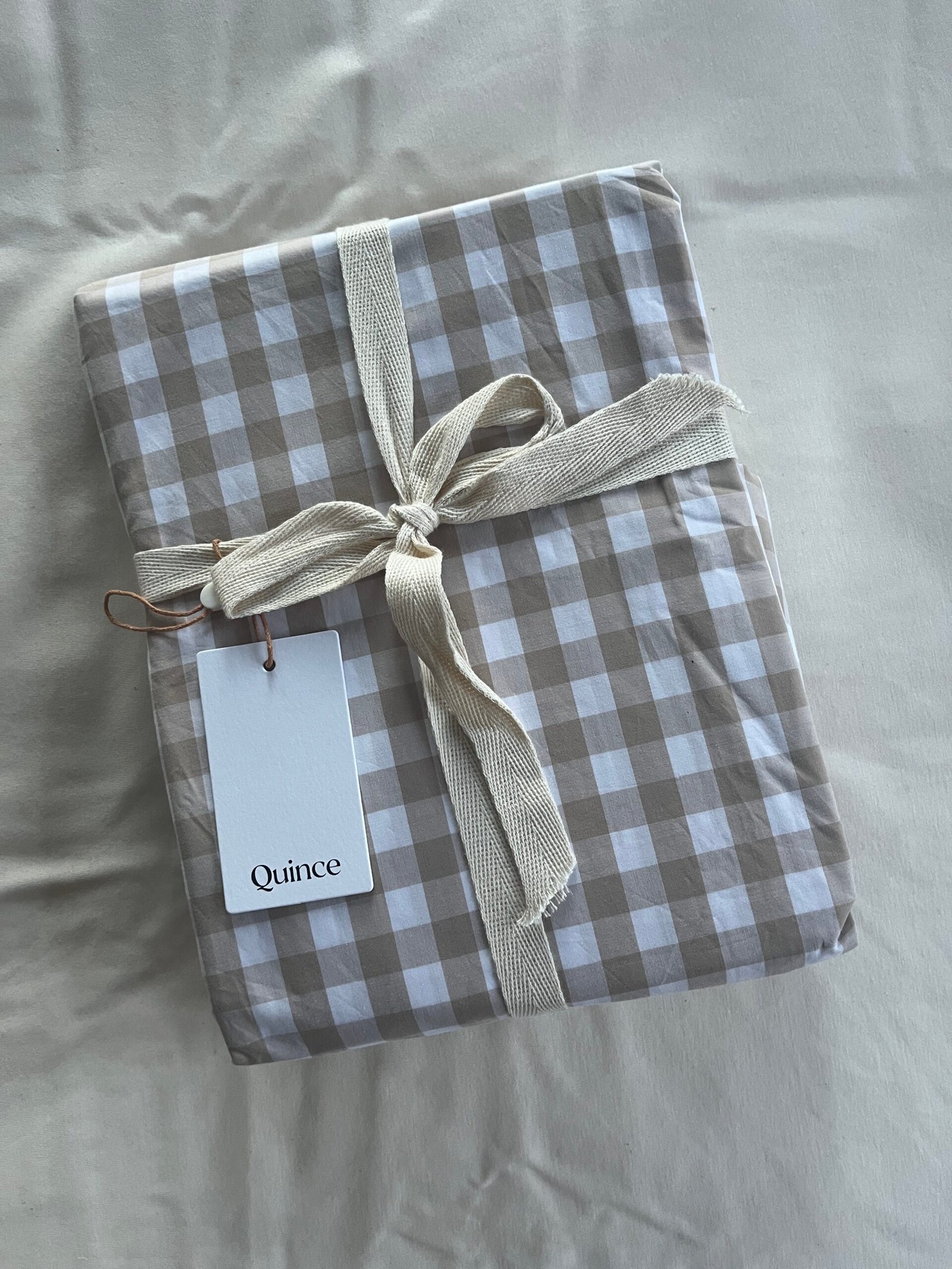 A package wrapped in checked fabric with a cream ribbon and a "Quince" tag on a plain background.