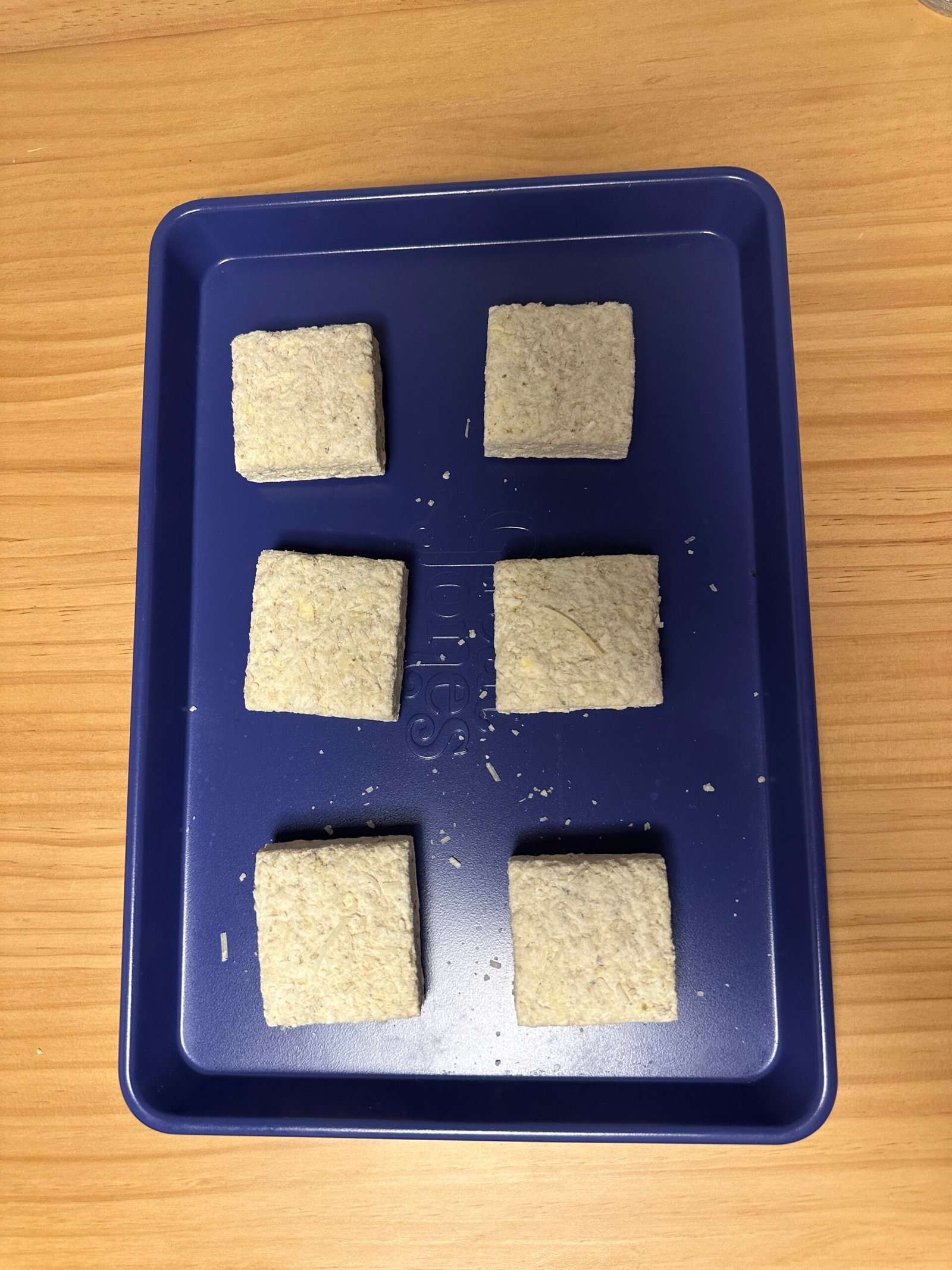 Six rectangular beige blocks on a blue tray placed on a wooden surface.