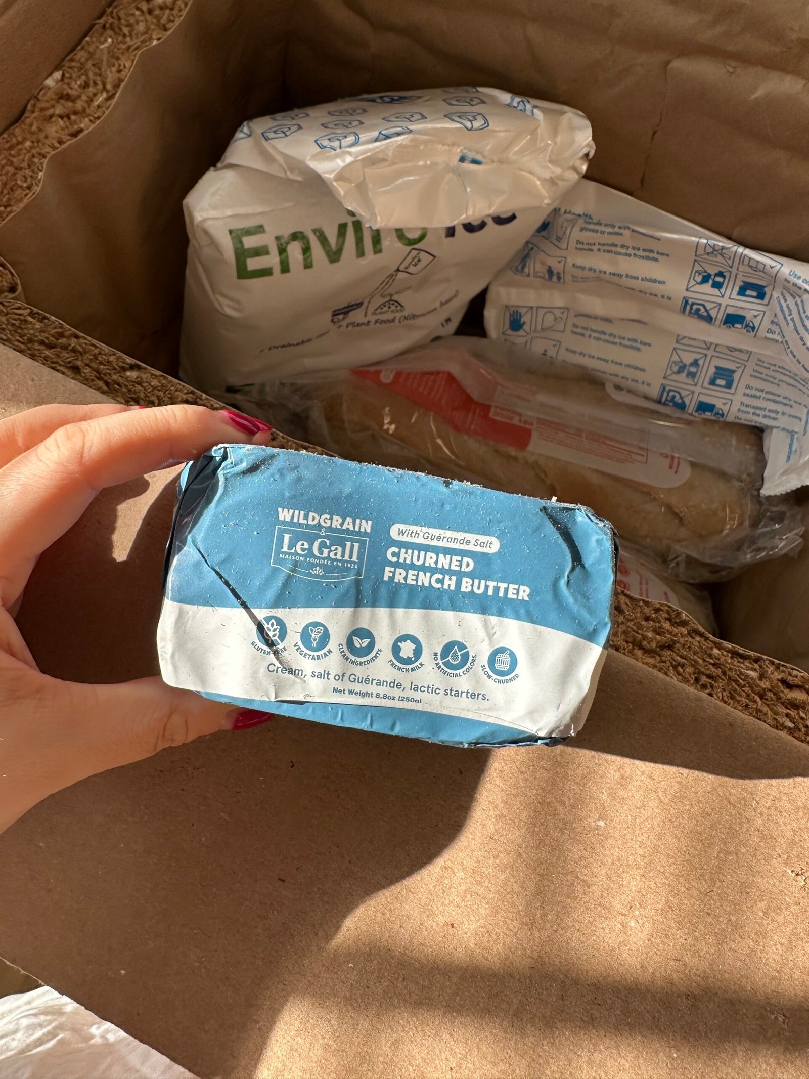 Person holding a package of Le Gall churned French butter in an open cardboard box with packing material and other items inside.