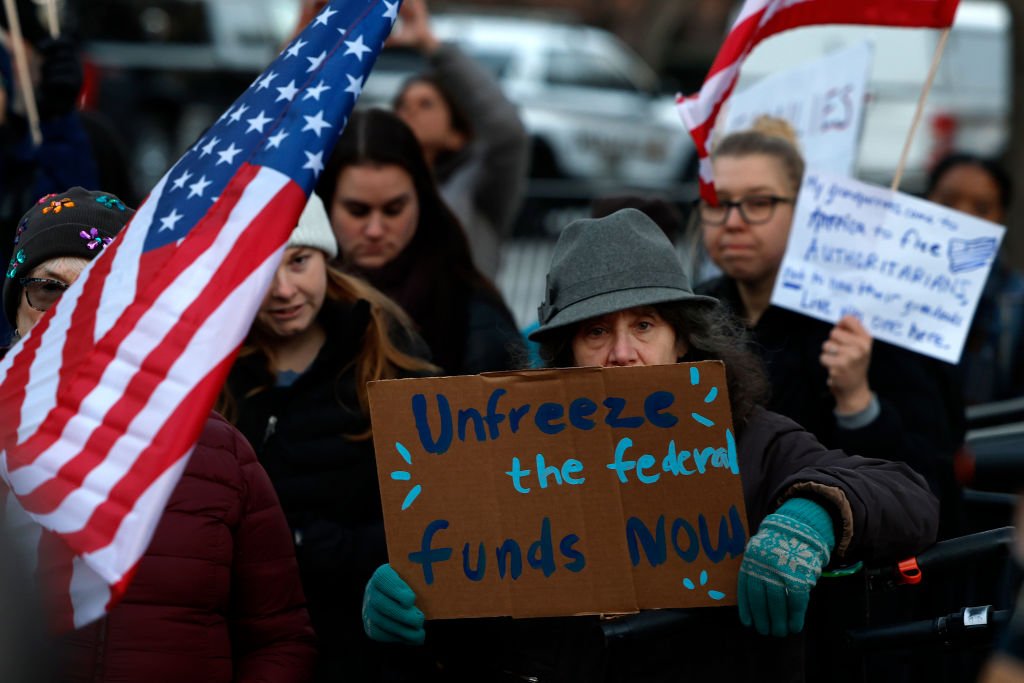 activists holding sign that says unfreeze the federal funds now