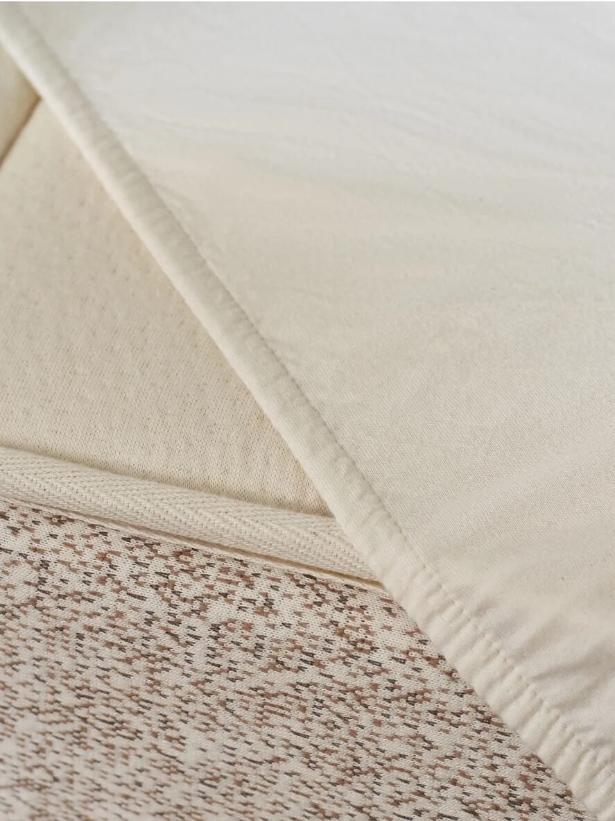 Close-up of a partially folded cream-colored mattress topper with textured and smooth sections, showing a speckled pattern on the lower layer.