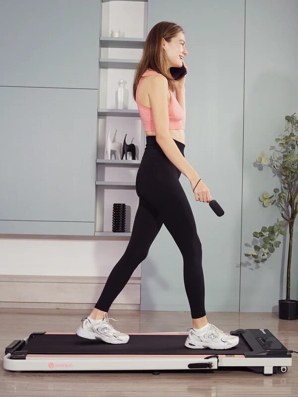 A woman in athletic wear walks on a treadmill while holding a remote.