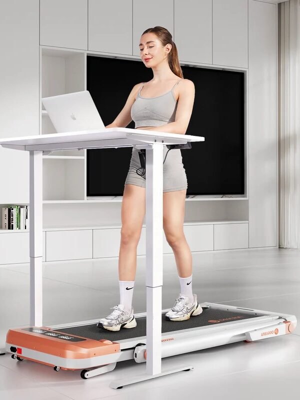 A woman exercises on a treadmill while working on a laptop at a standing desk in a modern room.