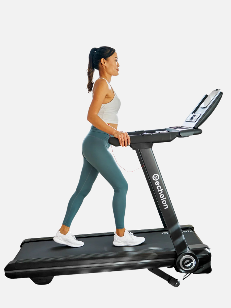 A woman in a light gray tank top and teal leggings is walking on a black Echelon treadmill, facing right.