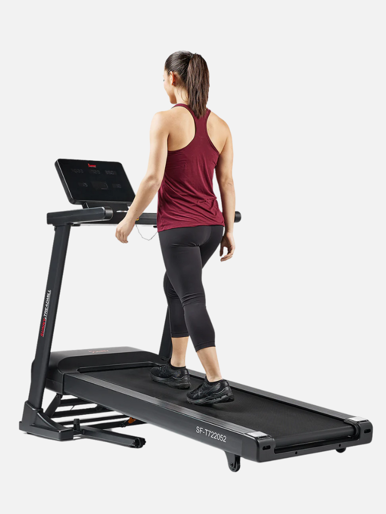 A person in athletic wear walks on a black treadmill with digital display.