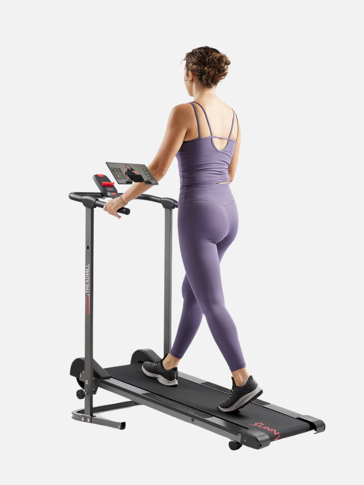 A woman in a purple workout outfit walks on a treadmill while using a tablet.