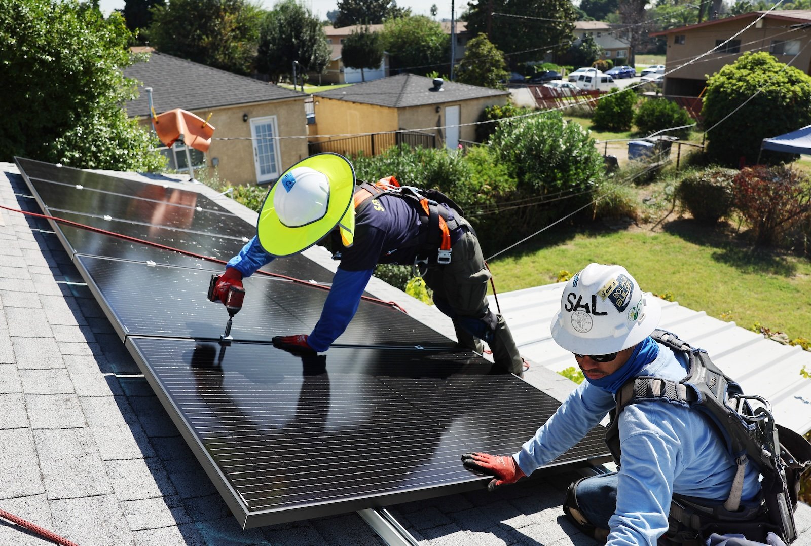 A photo of two workers installing solar panels on a roof