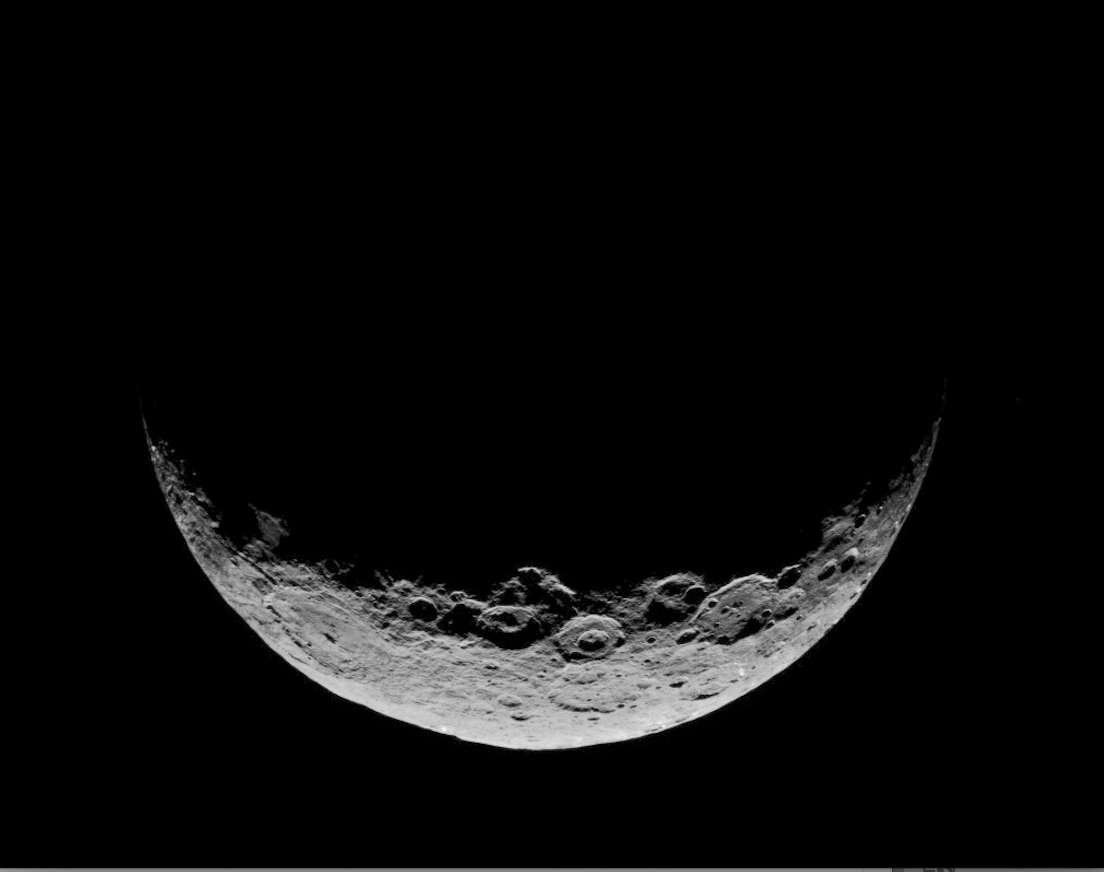 Ceres, a dwarf planet, appears as a gray, cratered crescent, as the spacecraft that took this image was on the planet's night side. Only the bottom of the planet is visible, with the rest indistinguishable from the darkness of space.