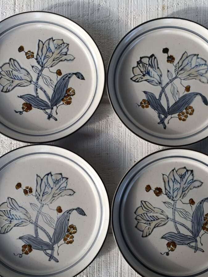 Four ceramic plates with floral designs arranged in a 2x2 grid on a wooden surface.