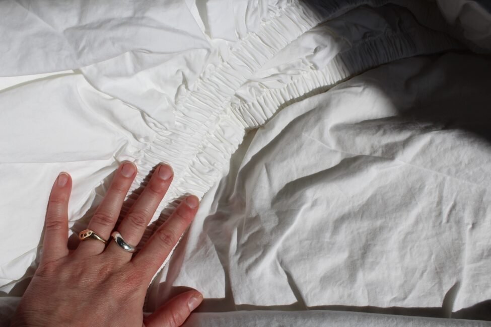 Hand with rings touching white gathered fabric.