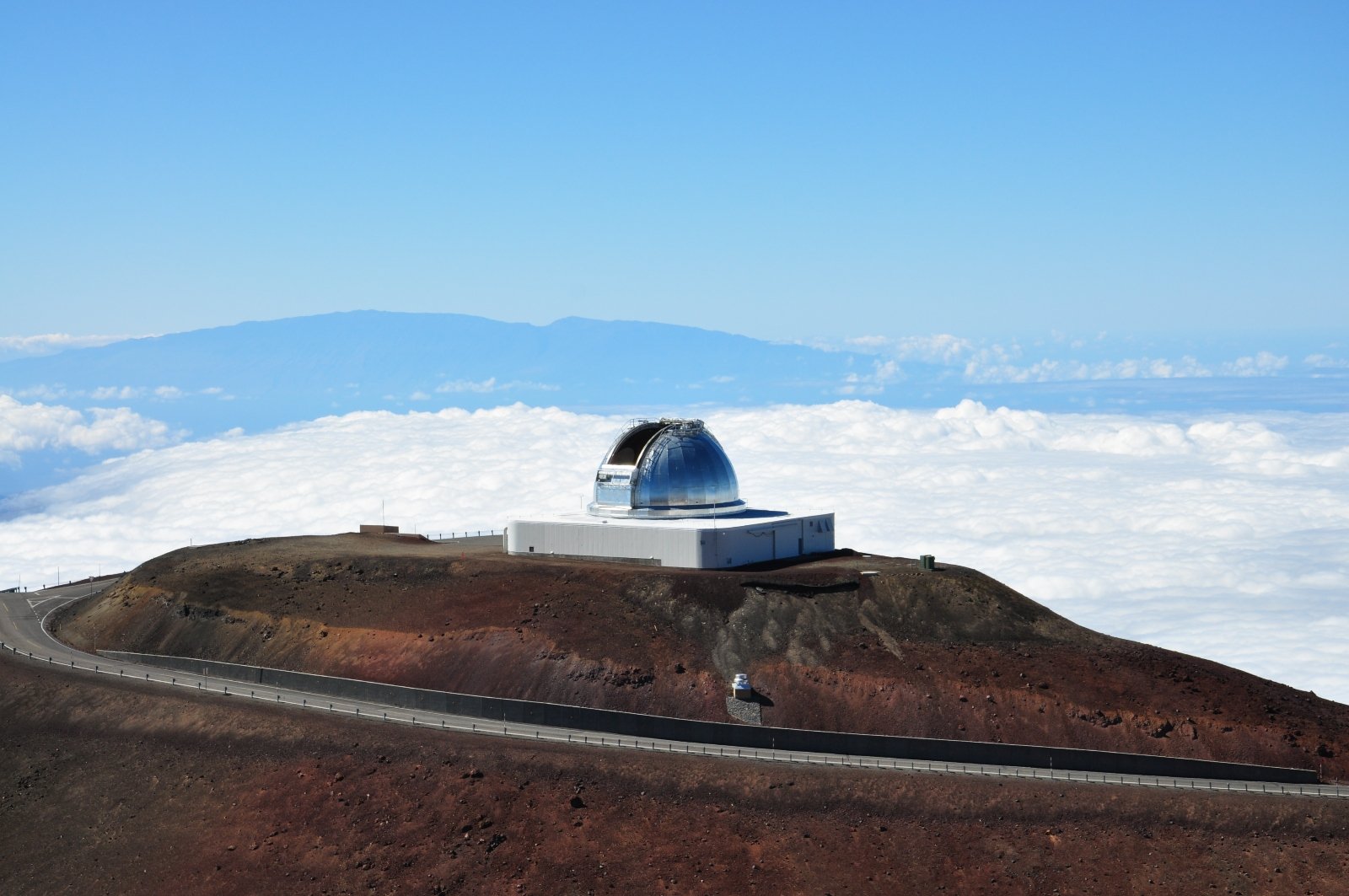 Observatory on top of Mauna Kea with the massive Mauna Loa in background and the clouds flowing through the valley between at a lower elevation.