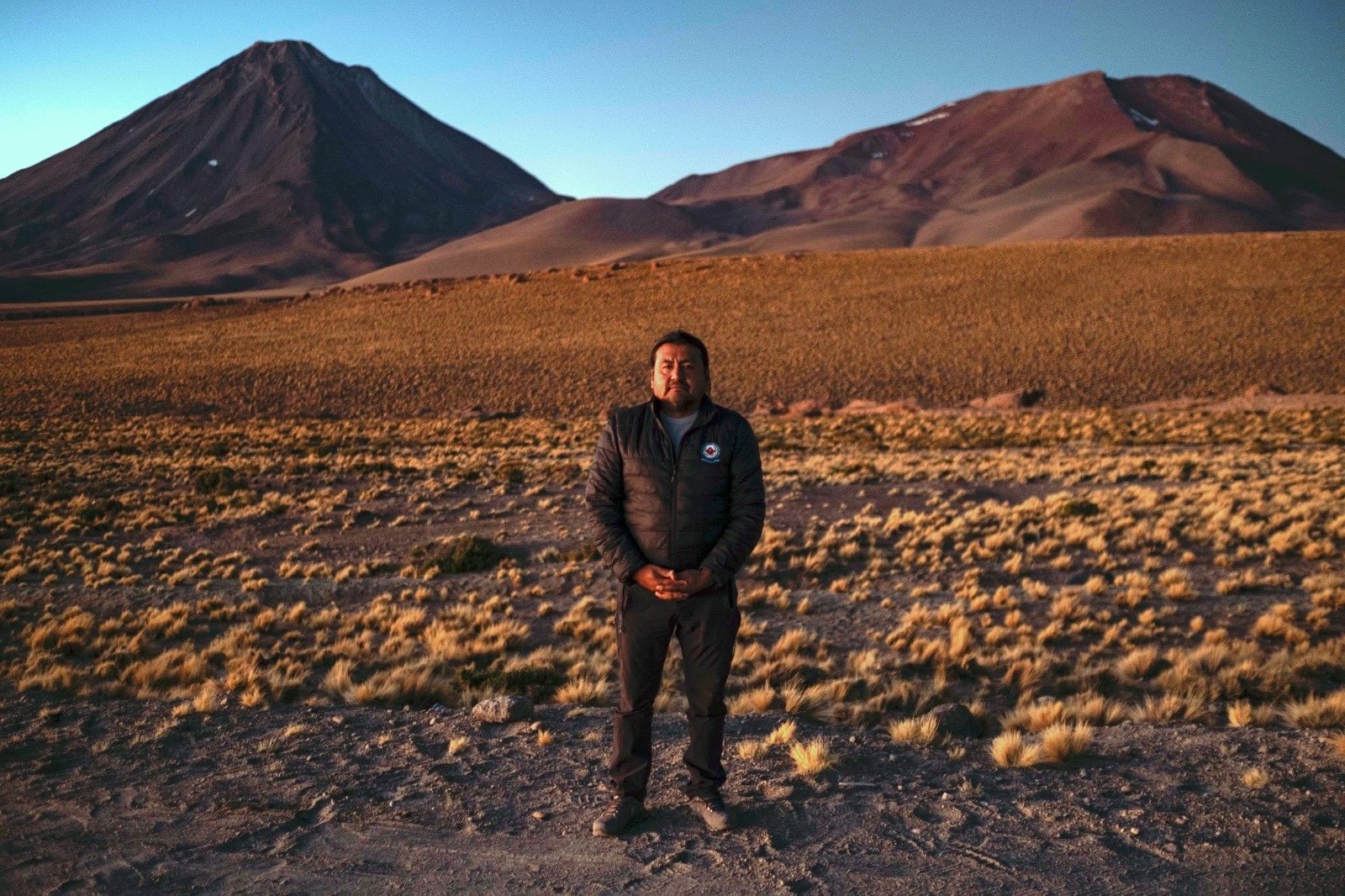 A man poses for a photo while standing in a large field with sparse vegetation