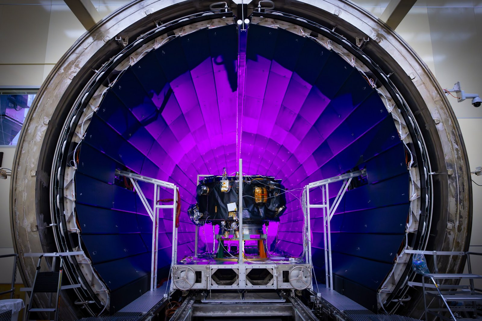 A tunnel dramatically lit in violet light dominates the photo. In front of it, a small spacecraft is on a track.