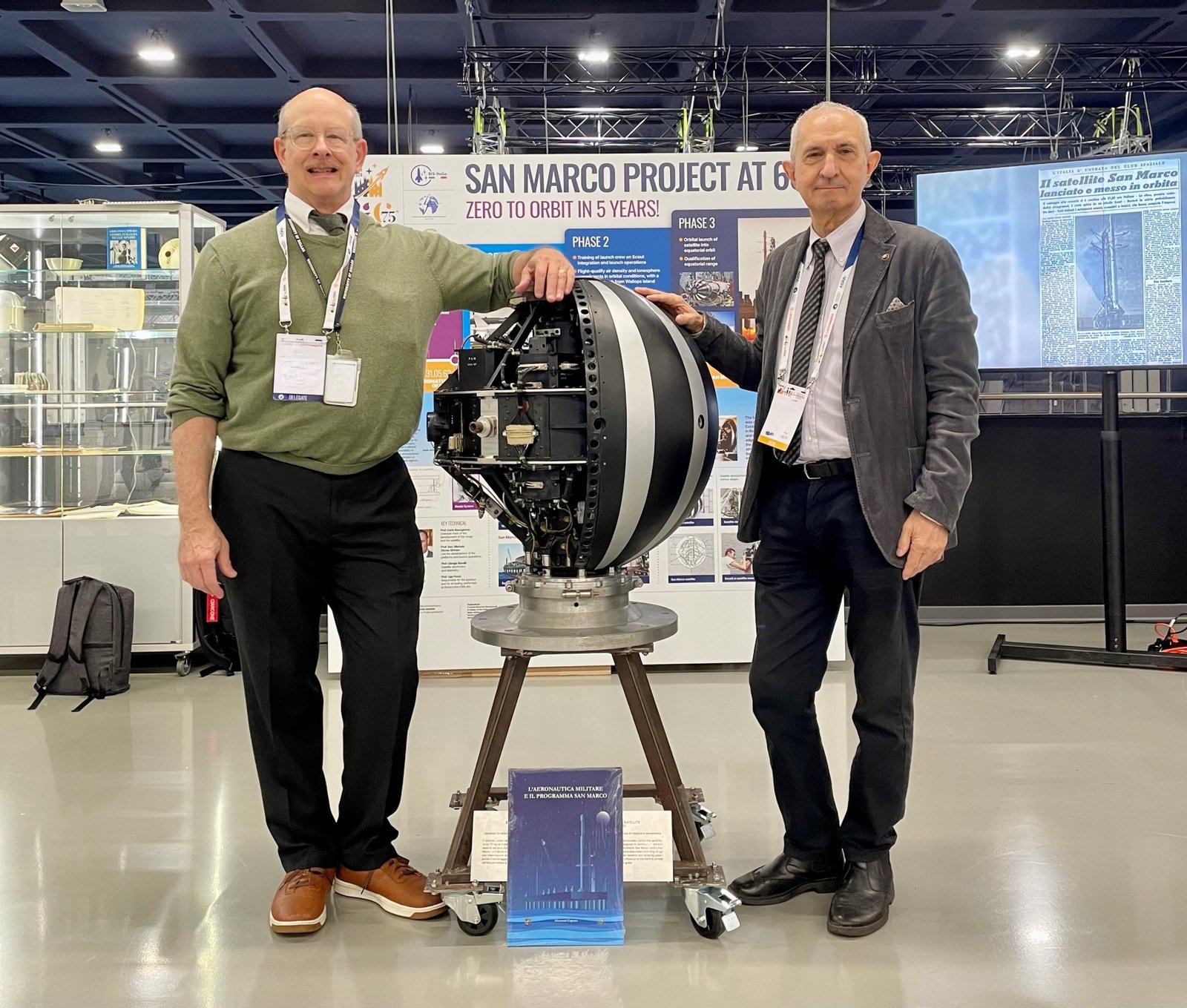 Two people pose in front of a spaceflight model at an exhibit.