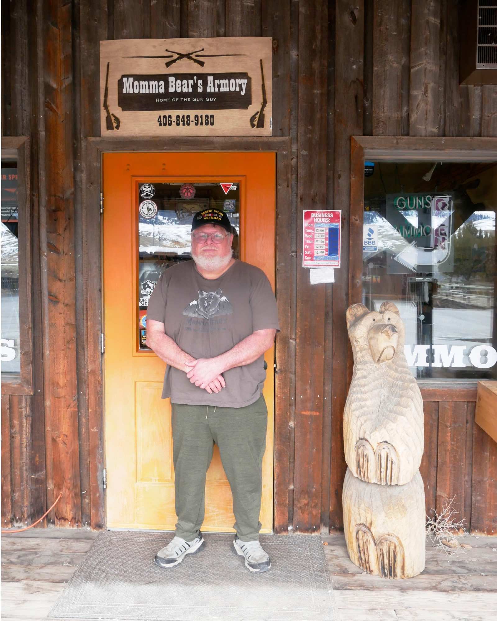 A man with a white beard and a baseball cap stands in front of a storefront labeled Mama Bear's Armory