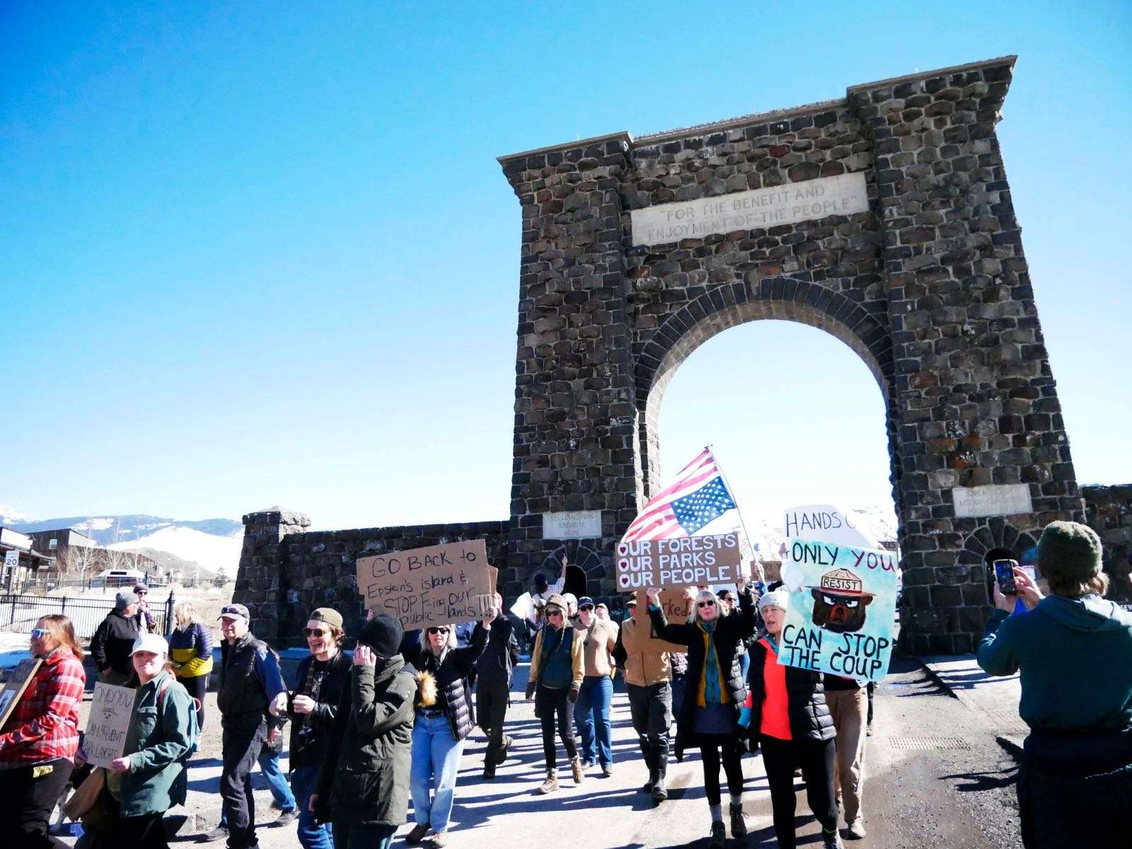 A crowd marches with signs beneath a stone arch
